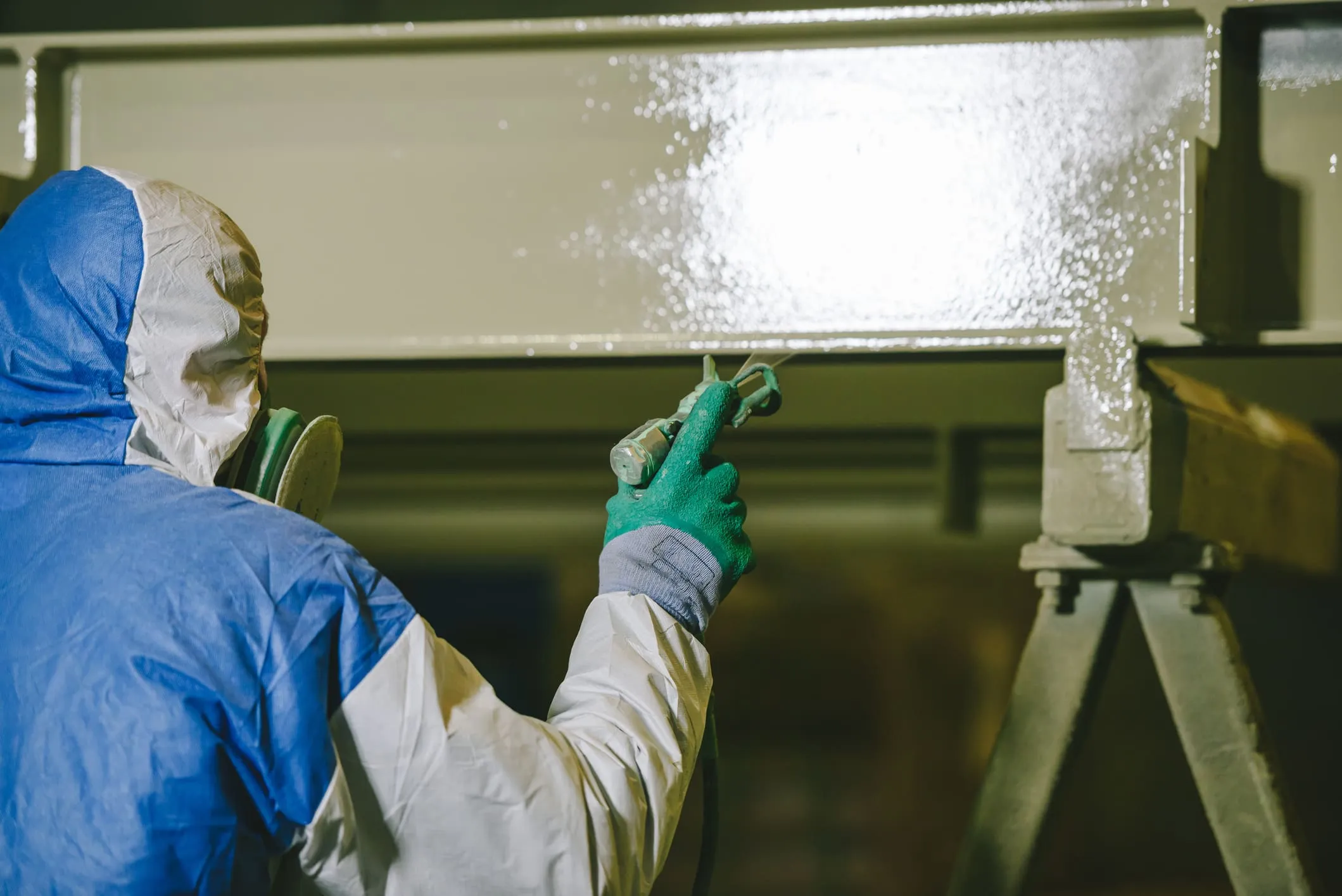 Worker in full PPE performing controlled hazardous coating removal on a steel structure